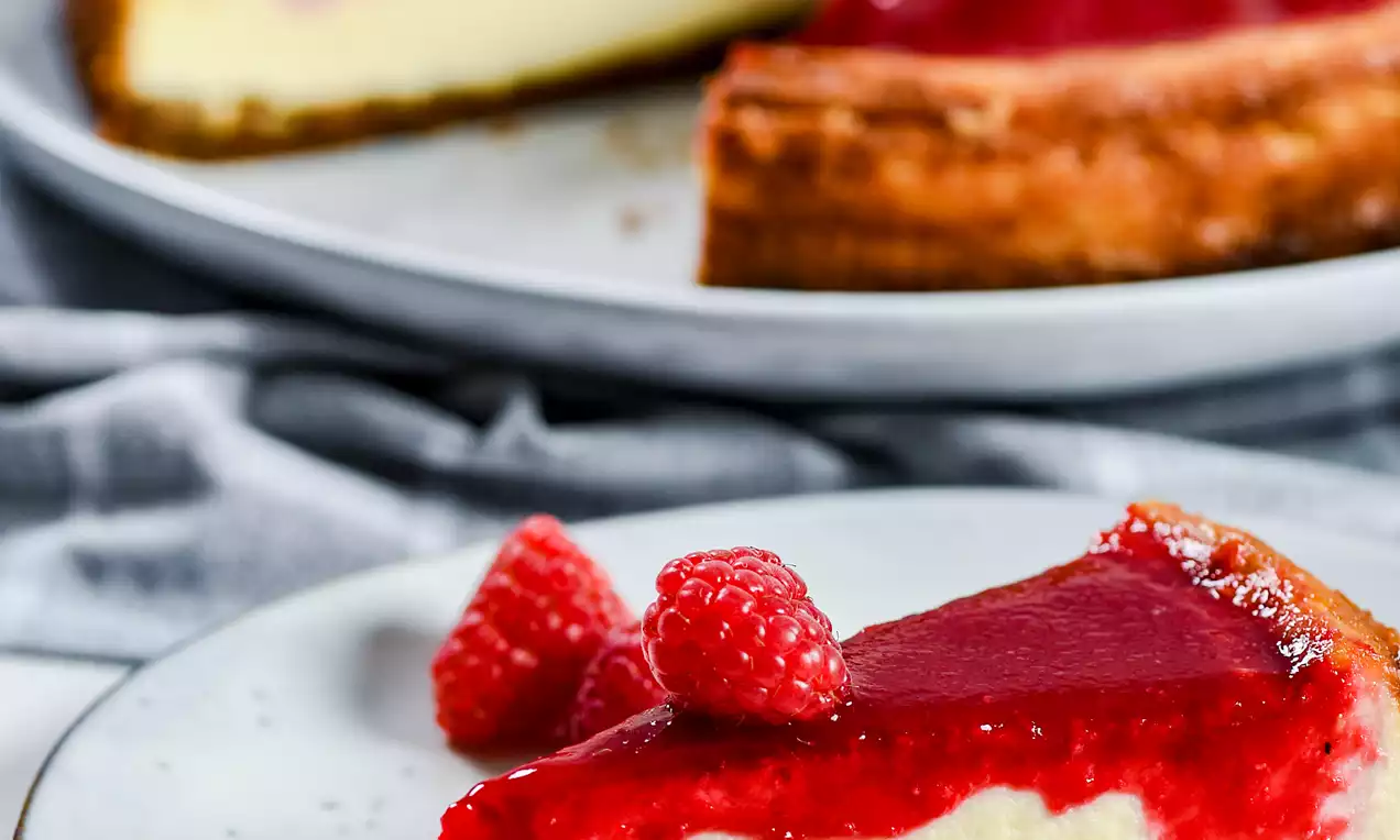 Picture - Bagt cheesecake med gyldenbrun kiksebund, flødefyld og blank hindbærgelé, pyntet med friske hindbær på lyse tallerkener